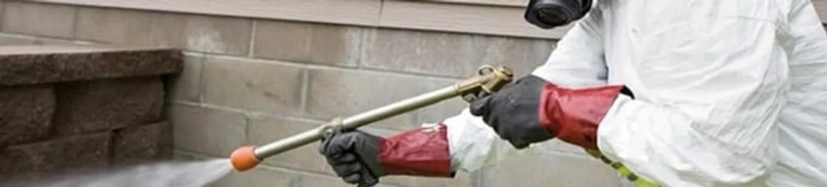 Pest control technician applying exterior insect treatment along a home foundation in Louisville, KY