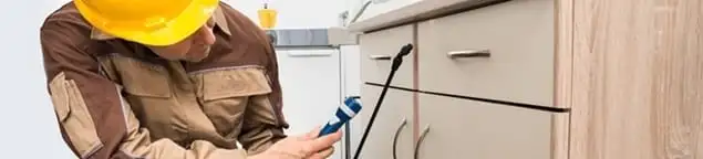 Roach exterminator applying treatment under kitchen cabinets in Louisville, KY