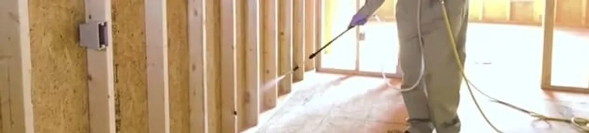 Termite treatment technician applying spray along framing and unfinished walls in Louisville, KY