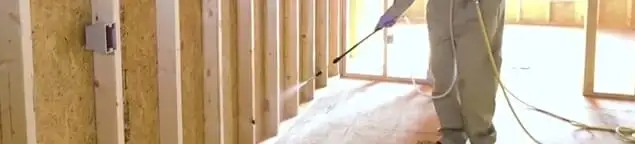 Termite treatment technician applying spray along framing and unfinished walls in Louisville, KY